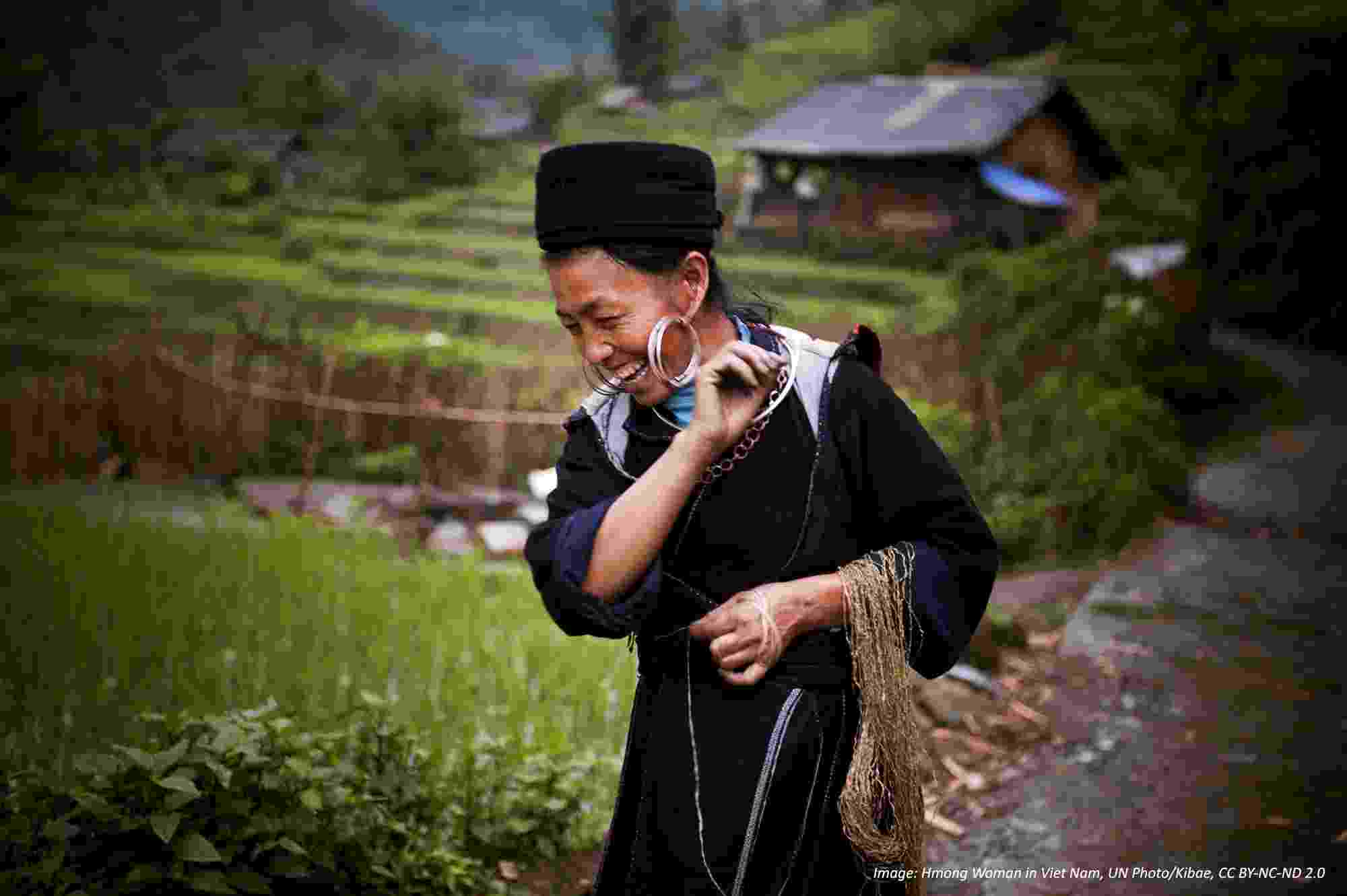 A Hmong hill tribe woman walks along a path between green rice paddy fields, whilst at work in Sin Chai, Viet Nam.